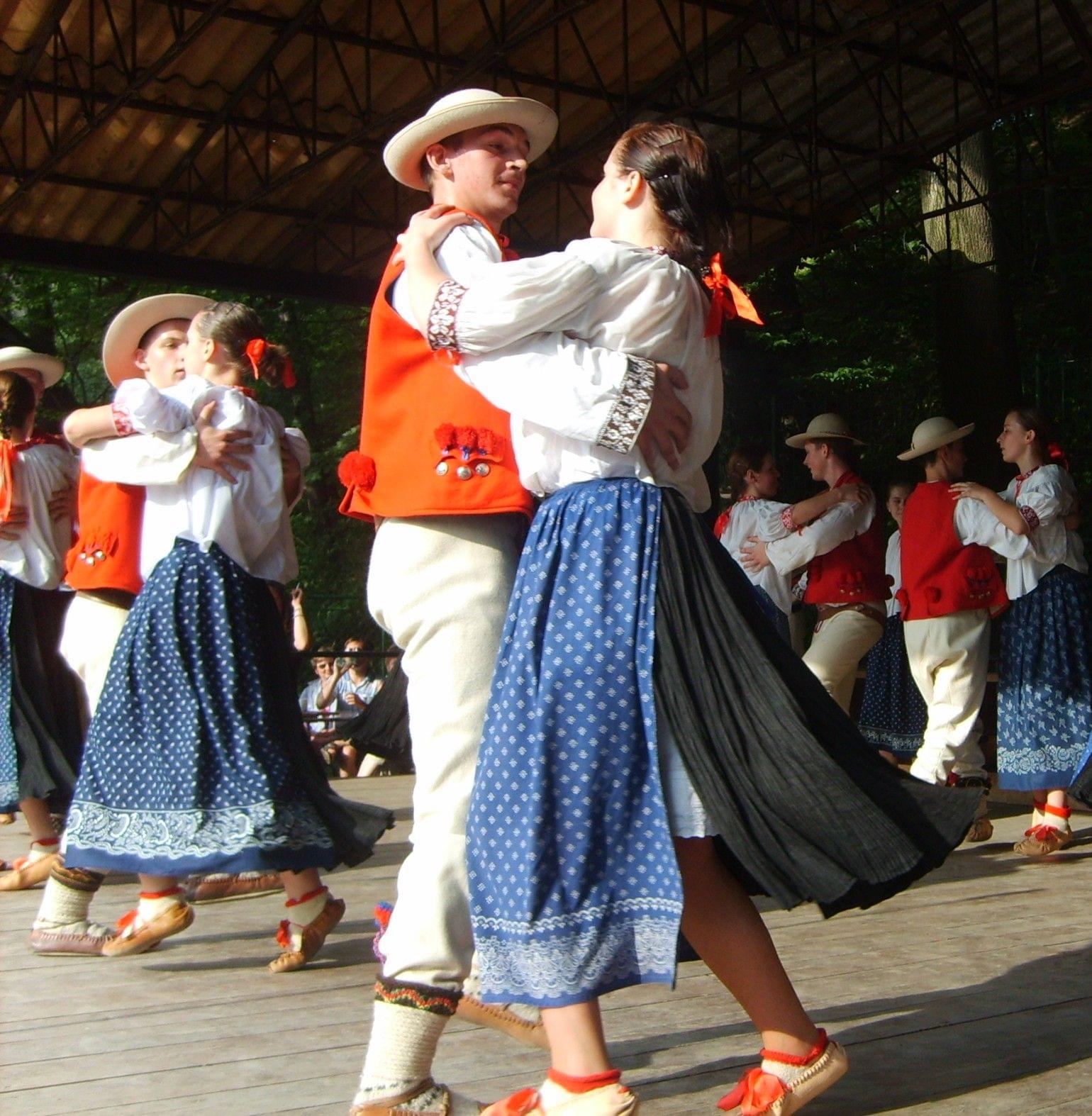 Kilka par góralskich w tradycyjnych strojach tańczących na drewnianej scenie.