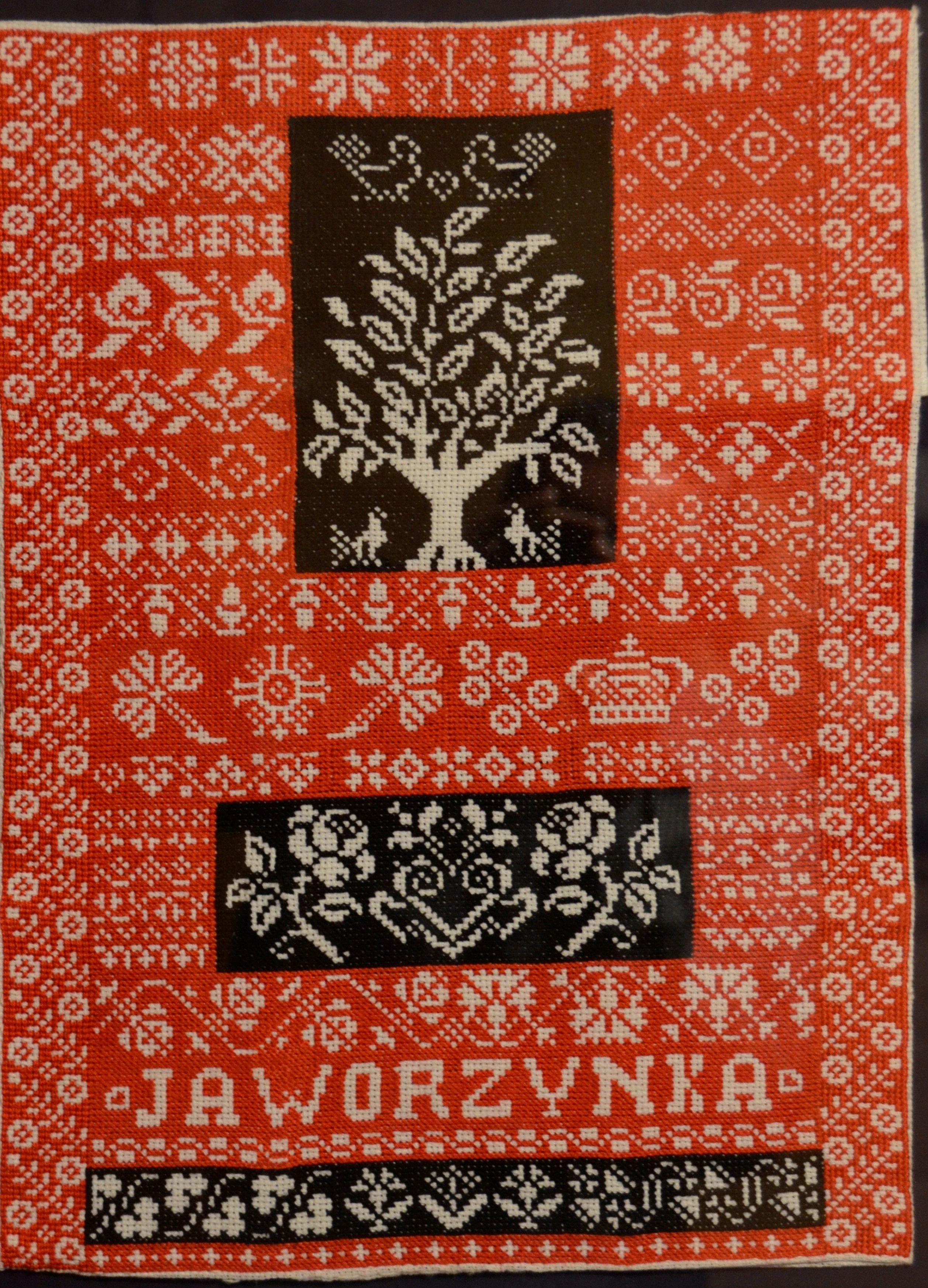 Fragment czerwono-biało-brązowego materiału z wyhaftowanym motywem ptaków, drzewa, róż i
napisem Jaworzynka.