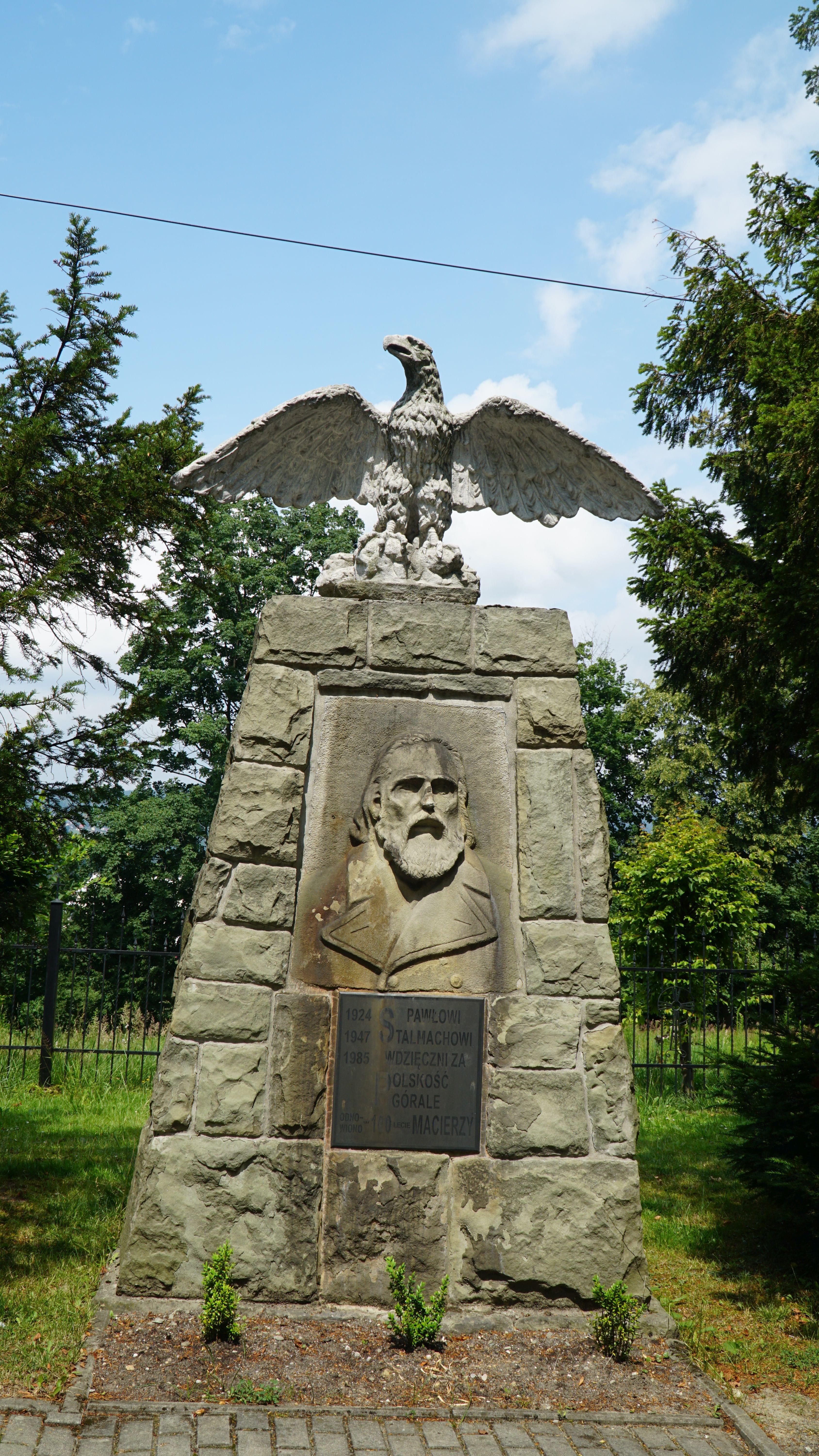 Kamienny pomnik Pawła Stalmacha wraz z popiersiem i pamiątkową tablicą. Obiekt zwieńczony jest
rzeźbionym sokołem. W tle płot starego cmentarza.